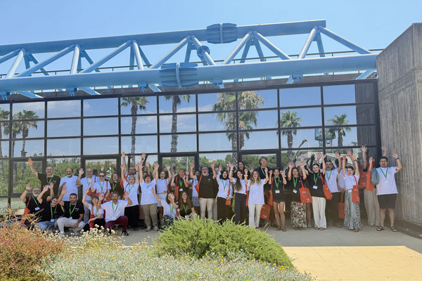 Group photo in front of a glasshouse reflecting palms and people cheering.