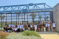 Group photo in front of a glasshouse reflecting palms and people cheering.